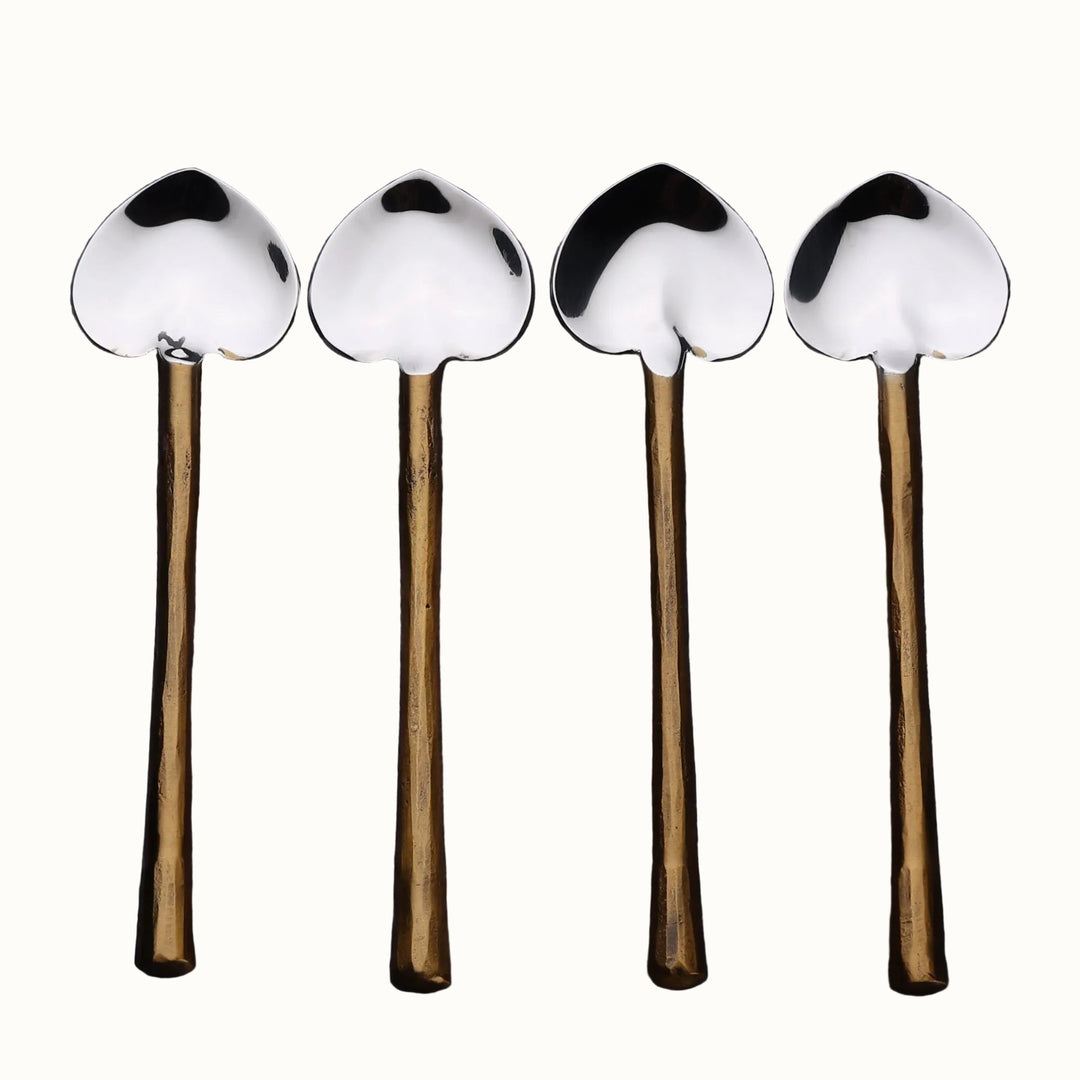Four heart spoons with metal handles and metal ends on a wooden surface