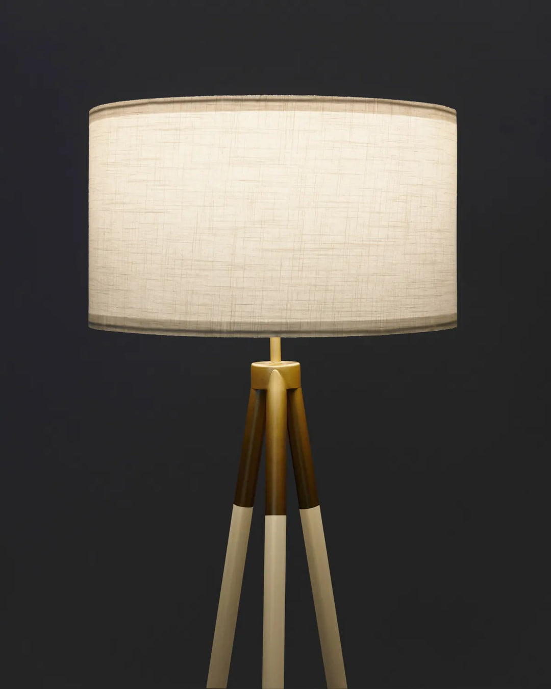 A modern tripod floor lamp with a large drum shade made of textured cream linen fabric, supported by three wooden legs that transition from dark brown to light beige at the joints, set against a dark charcoal background.