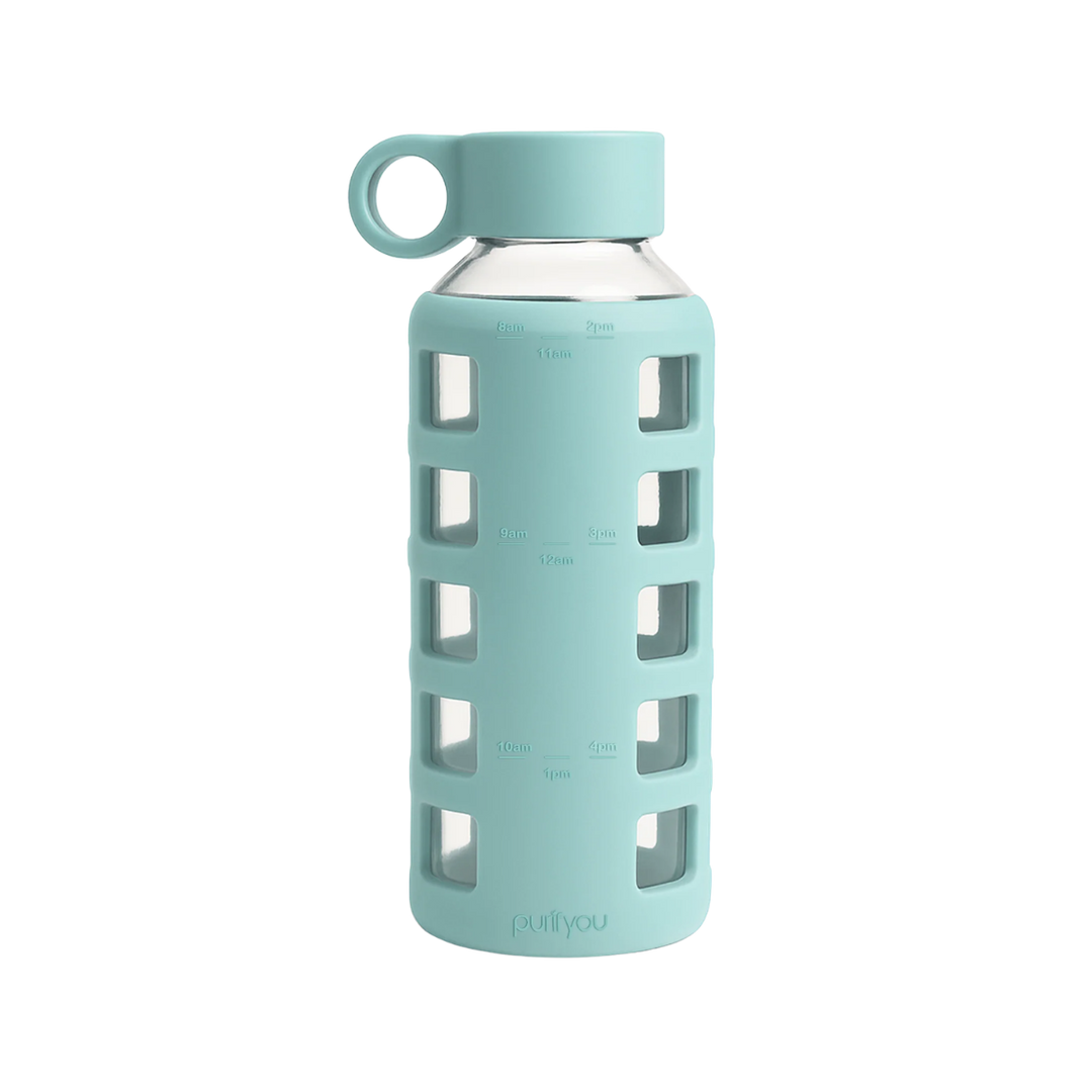 A mint green glass water bottle with a matching silicone sleeve featuring square cutouts, a matching silicone cap with a loop handle, and measurement markings on the sleeve.