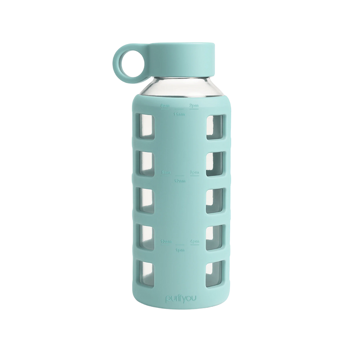 A mint green glass water bottle with a matching silicone sleeve featuring square cutouts, a matching silicone cap with a loop handle, and measurement markings on the sleeve.