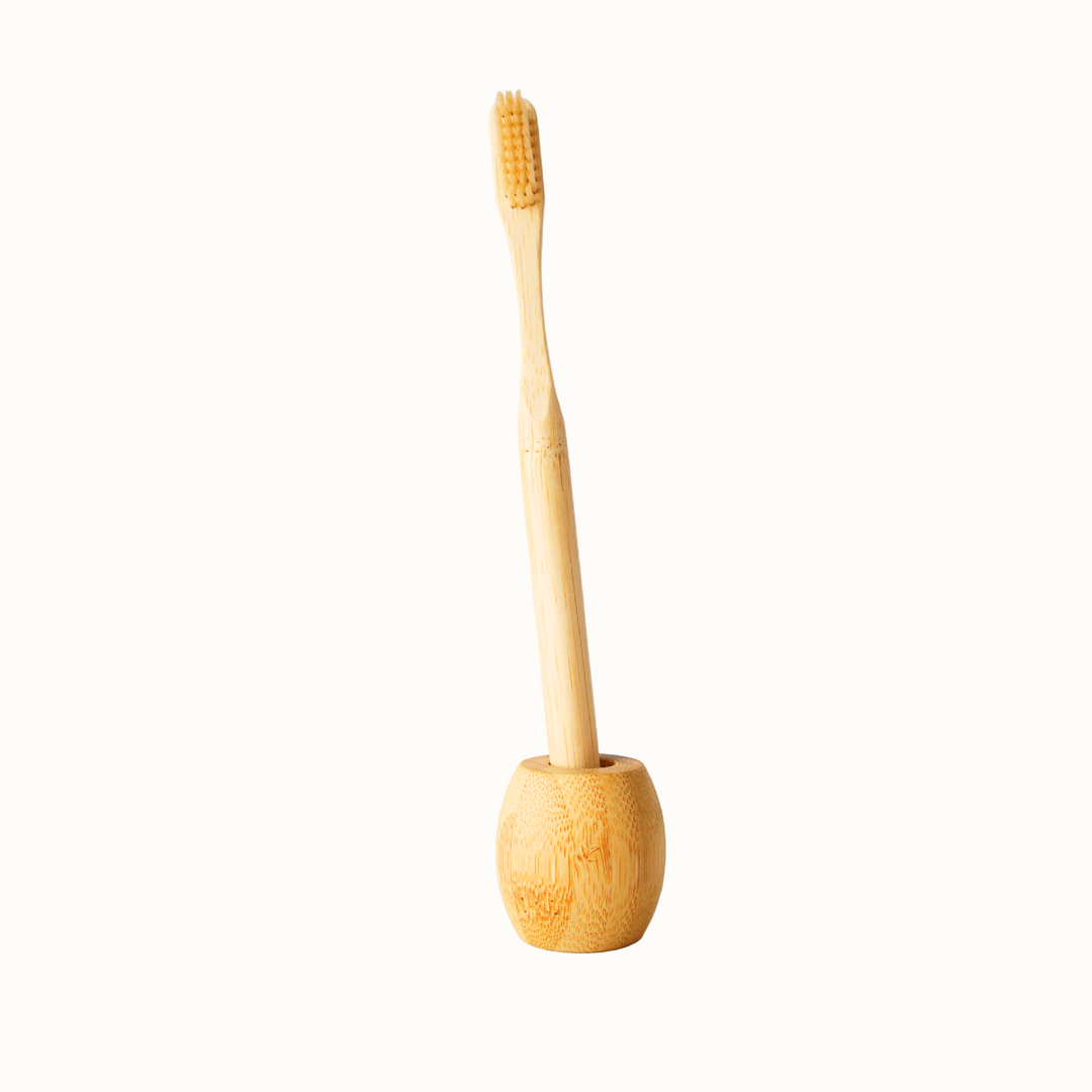 Bamboo toothbrush in a wooden holder against a light gray tiled wall.